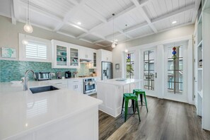 A modern kitchen with white cabinetry, a large island, and a view to the outside. - The Sand Trap | Pet Friendly | Steps to Beach (Port Aransas)