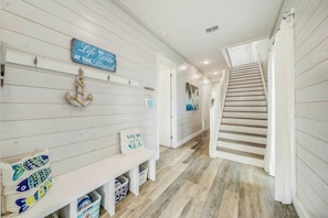 A hallway with a wooden floor, a staircase, and various wall decorations including a sign that says 'Life is good at the beach.' - The Sand Trap | Pet Friendly | Steps to Beach (Port Aransas)