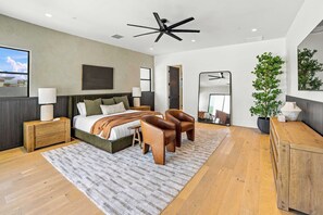 A modern bedroom with a bed, nightstands, a mirror, a ceiling fan, and a large window. - HÓZHÓ| Golf Simulator, Theatre & Pickleball & Pool (Scottsdale)
