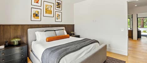 Un dormitorio moderno con una cama, mesitas de noche, ventilador de techo y obras de arte enmarcadas en la pared.