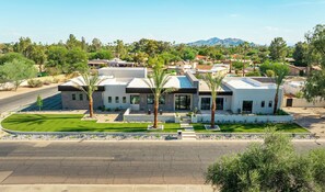 A modern two-story house with a flat roof, surrounded by a well-maintained lawn and palm trees. - HÓZHÓ| Golf Simulator, Theatre & Pickleball & Pool (Scottsdale)