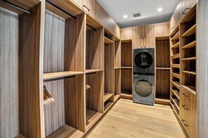 A walk-in closet with wooden shelving, a built-in washer, and a mirrored closet door. - HÓZHÓ| Golf Simulator, Theatre & Pickleball & Pool (Scottsdale)