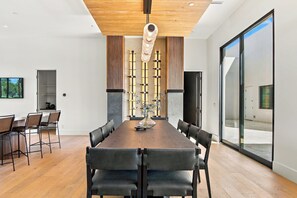 A modern dining area with a long wooden table, black chairs, and a vase with flowers. - HÓZHÓ| Golf Simulator, Theatre & Pickleball & Pool (Scottsdale)
