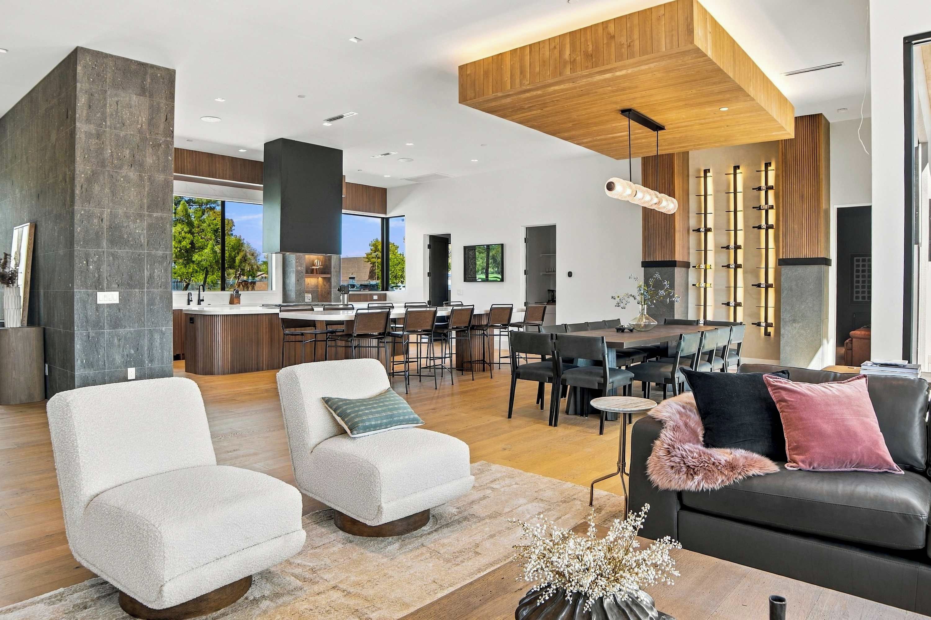 A modern living room with a fireplace, a dining area, and a kitchen with large windows.