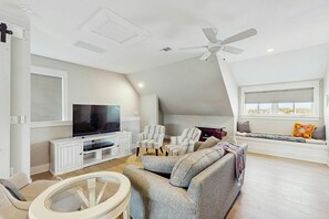 Ein modernes Wohnzimmer mit einem Flachbildfernseher, gestreiften Sesseln, einem grauen Sofa, einem Deckenventilator und einem Fenster mit Jalousien.