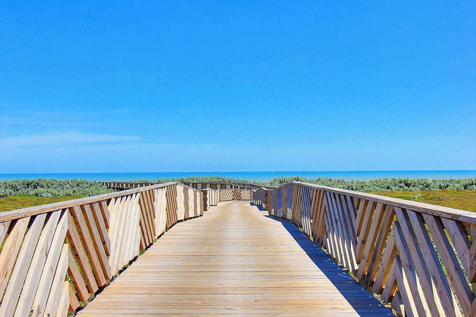 Une promenade en bois mène à une plage, avec un ciel bleu dégagé.