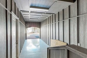 A corridor with wooden paneling and a polished floor, leading to an outdoor area with a bench and a tree. - Third Coast Charm | Pool Steps Away | Balconies (Port Aransas)