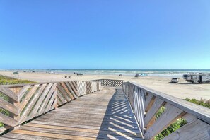 A wooden boardwalk leading to a beach with vehicles and a tent. - Third Coast Charm | Pool Steps Away | Balconies (Port Aransas)