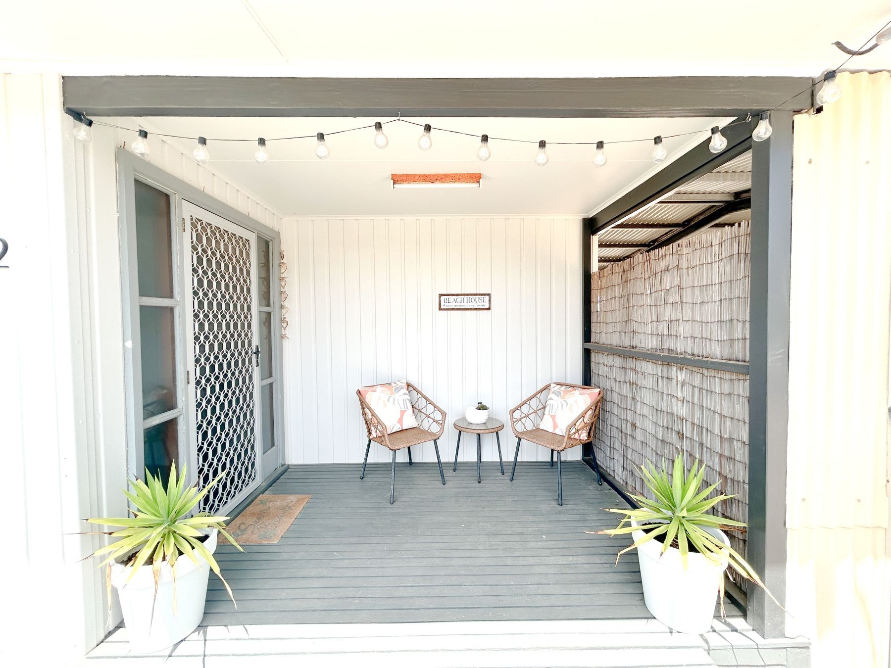 A porch with two wicker chairs, a small table, and string lights.