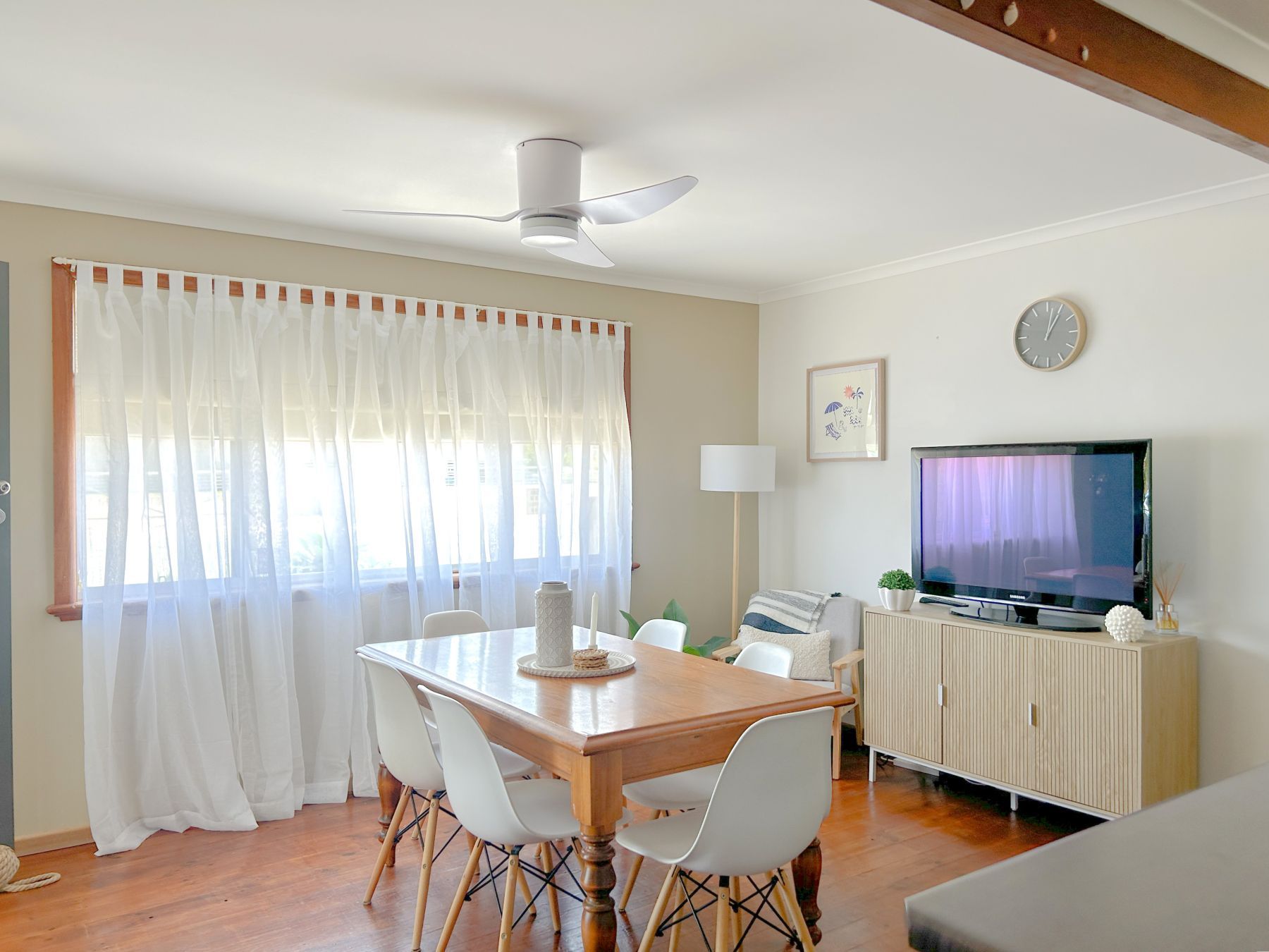 A dining area with a table, chairs, a ceiling fan, a television, and a clock on the wall.
