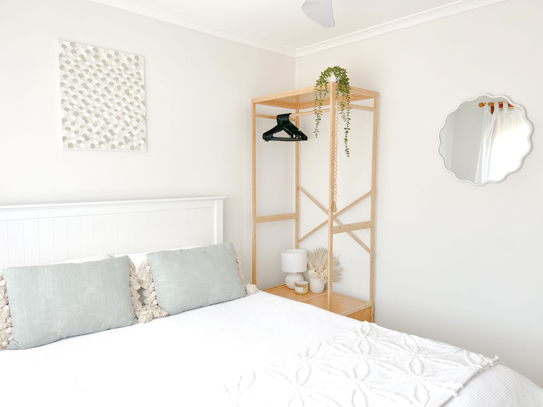 A bedroom with a bed, a bedside table with a lamp, a mirror, and a wall-mounted shelf with a plant.