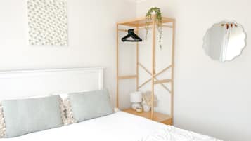 Une chambre à coucher avec un lit, une table de chevet avec une lampe, un miroir et une étagère fixée au mur, sur laquelle se trouve une plante.