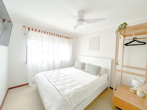 A bedroom with a bed, a ceiling fan, a window with curtains, a wall-mounted light, and a wooden shelf with a hanging garment. - Bliss at the Bay, Moonta Bay (Moonta Bay)