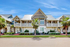 A multi-story hotel with a central atrium, balconies, and a well-maintained lawn. - Belle Beach Home | Steps to Beach | Game Room (Port Aransas)