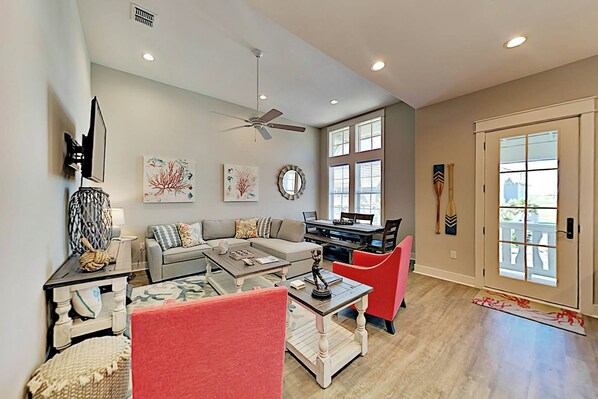 A living room with a sofa, coffee table, and a dining table. There are ceiling fans and recessed lighting. - Belle Beach Home | Steps to Beach | Game Room (Port Aransas)