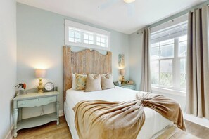 A bedroom with a large bed, two bedside tables, a wooden headboard, and a window with curtains. - Belle Beach Home | Steps to Beach | Game Room (Port Aransas)