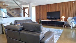 Un salon moderne avec un canapé en cuir, un téléviseur à écran plat fixé à un mur en bois et un escalier menant à un niveau supérieur.