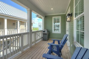 Eine überdachte Veranda mit Grill, zwei blaue Adirondack-Stühle und einem weißen Geländer.