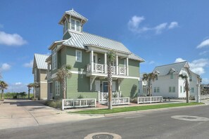 A two-story house with a balcony, a small tower-like structure on the roof, and a well-maintained lawn. - Green Turtle Cottage | Steps to Beach and Resort (Port Aransas)