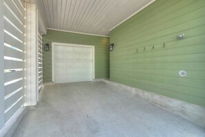 A hallway with a garage door, a concrete floor, and a green wall with a metal door handle. - Green Turtle Cottage | Steps to Beach and Resort (Port Aransas)