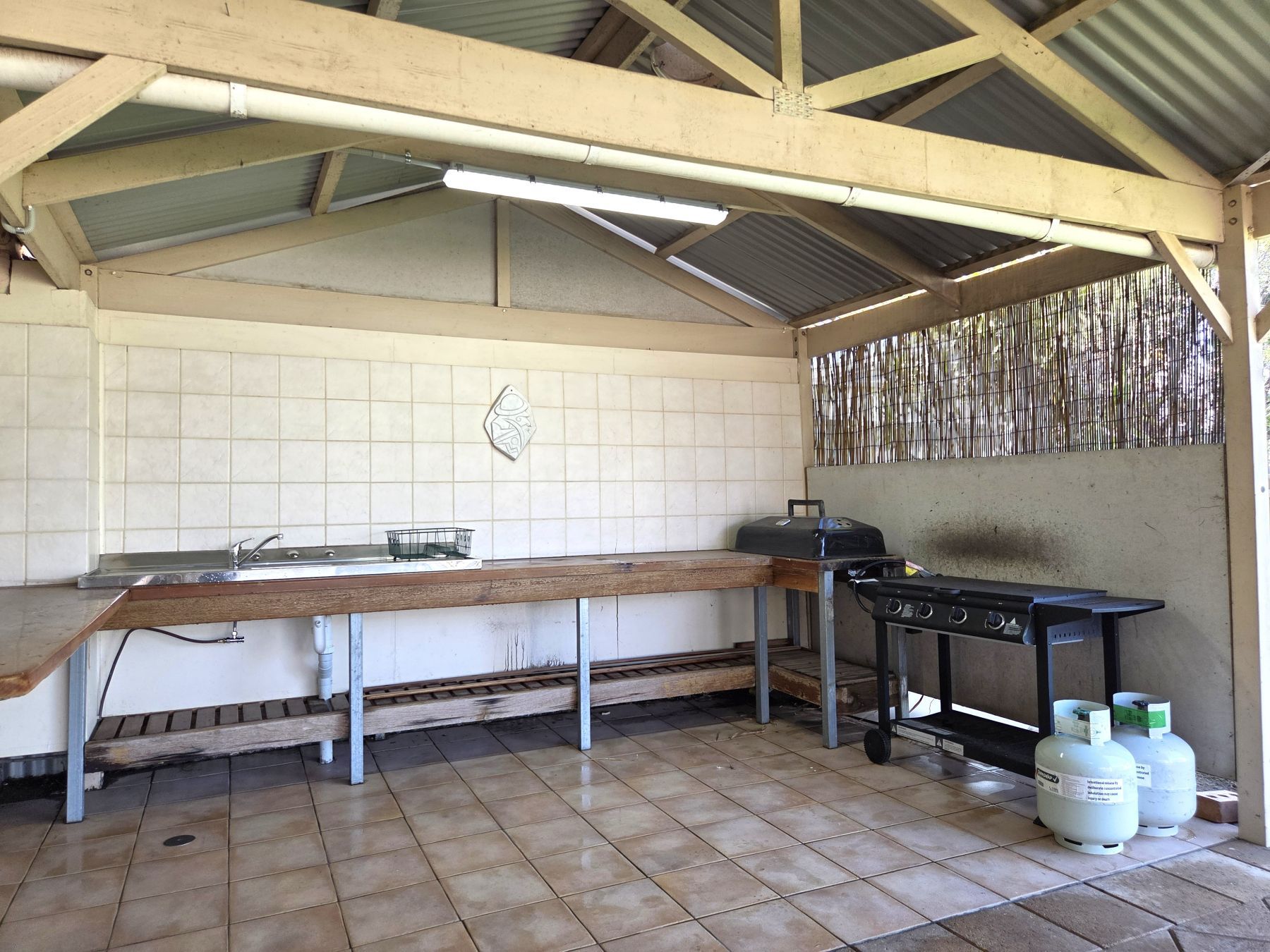 A kitchen with a tiled backsplash, a sink, a wooden countertop, a grill, and propane tanks.