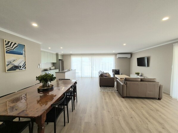 A modern apartment with a dining area, kitchen, living room, and a large window.