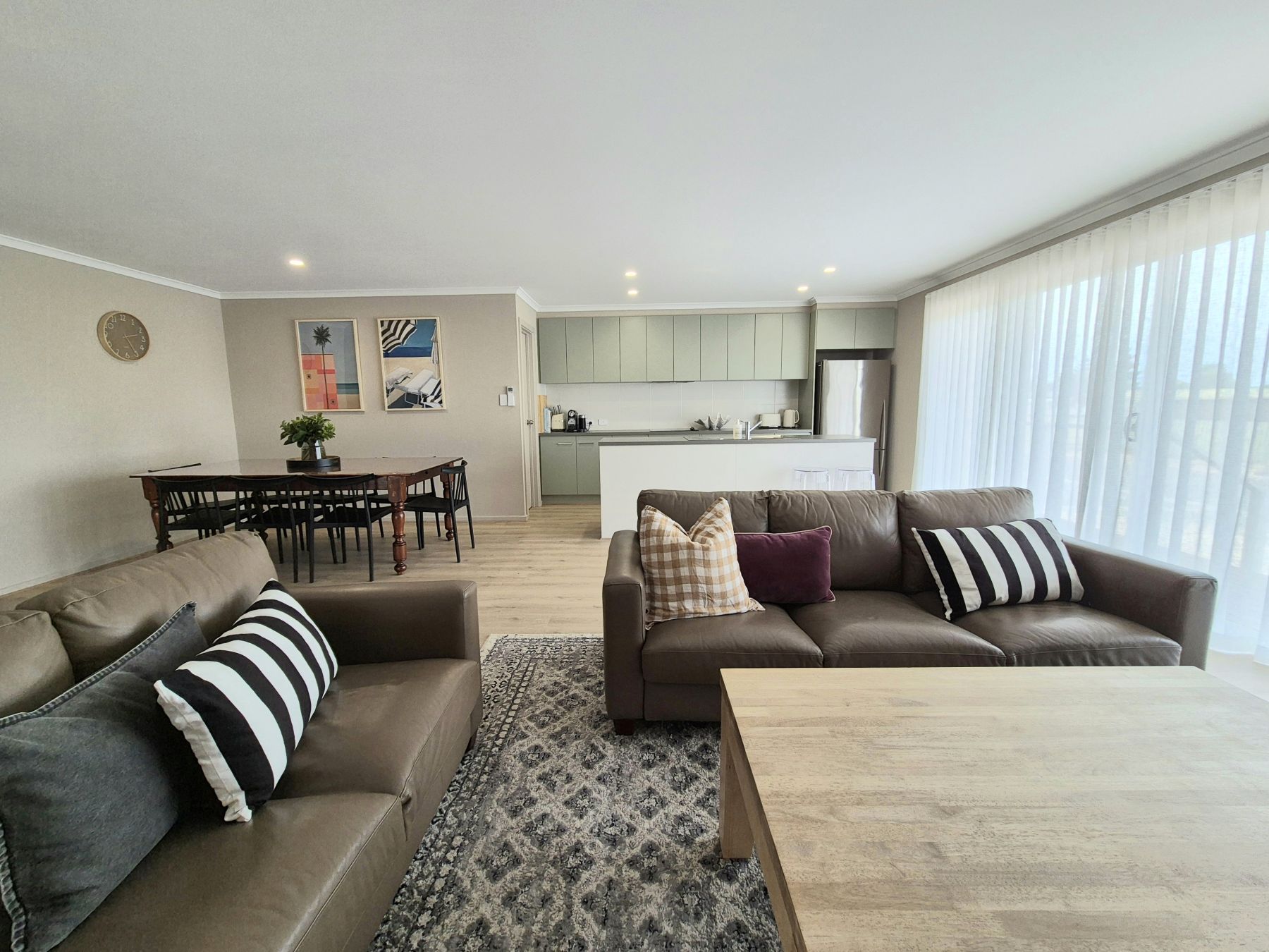 A modern living room with a sofa, coffee table, and a dining area with chairs and a table.
