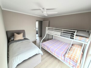 A bedroom with a single bed, a bunk bed, a ceiling fan, and a door leading to another room.