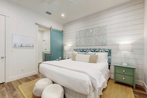 Quarto com cama, mesas de cabeceira, um criado-mudo, janela com persianas e parede com mapas.