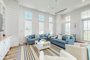 A spacious living room with a sectional sofa, a coffee table, and a view of the outdoors through large windows. - Silverado Waves | Steps to Beach |Resort Amenities (Port Aransas)