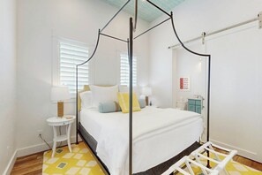 Een slaapkamer met een hemelbed, een nachtkastje met een lamp, een klein krukje en een wandplank.