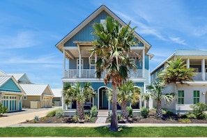 A two-story house with a balcony, surrounded by palm trees and a well-maintained lawn. - Silverado Waves | Steps to Beach |Resort Amenities (Port Aransas)