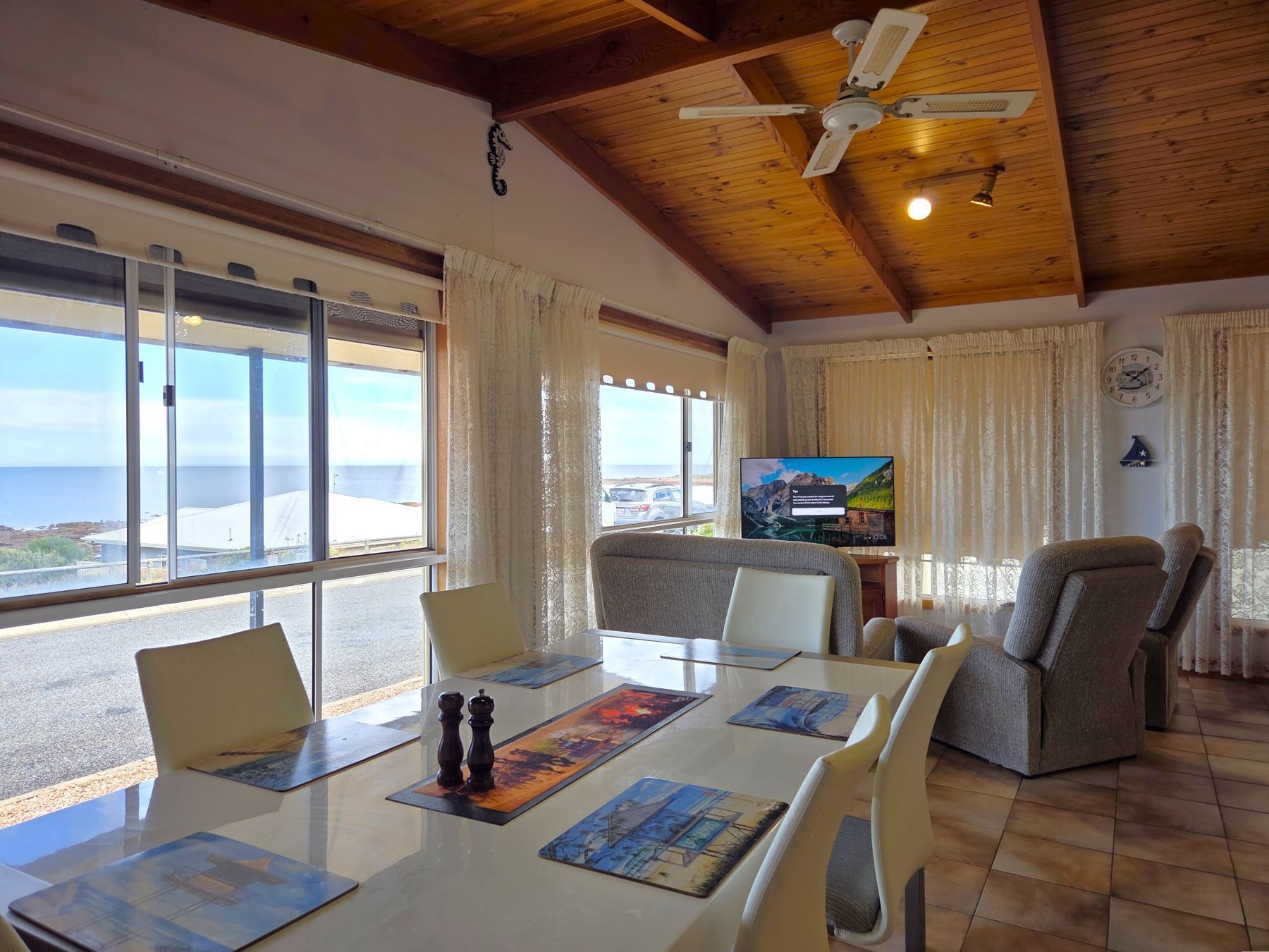 A dining area with a view of the sea, a television, and a clock on the wall.