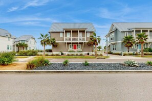A residential building with a two-story structure, a red front door, and a balcony. - Silverado Waves | Golf Views | Steps to Beach (Port Aransas)