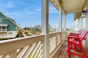 A balcony with a view of a coastal residential area, featuring a wooden railing and red Adirondack chairs. - Silverado Waves | Golf Views | Steps to Beach (Port Aransas)