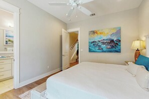 A bedroom with a bed, a painting, a lamp, and a staircase leading to another room. - Silverado Waves | Golf Views | Steps to Beach (Port Aransas)