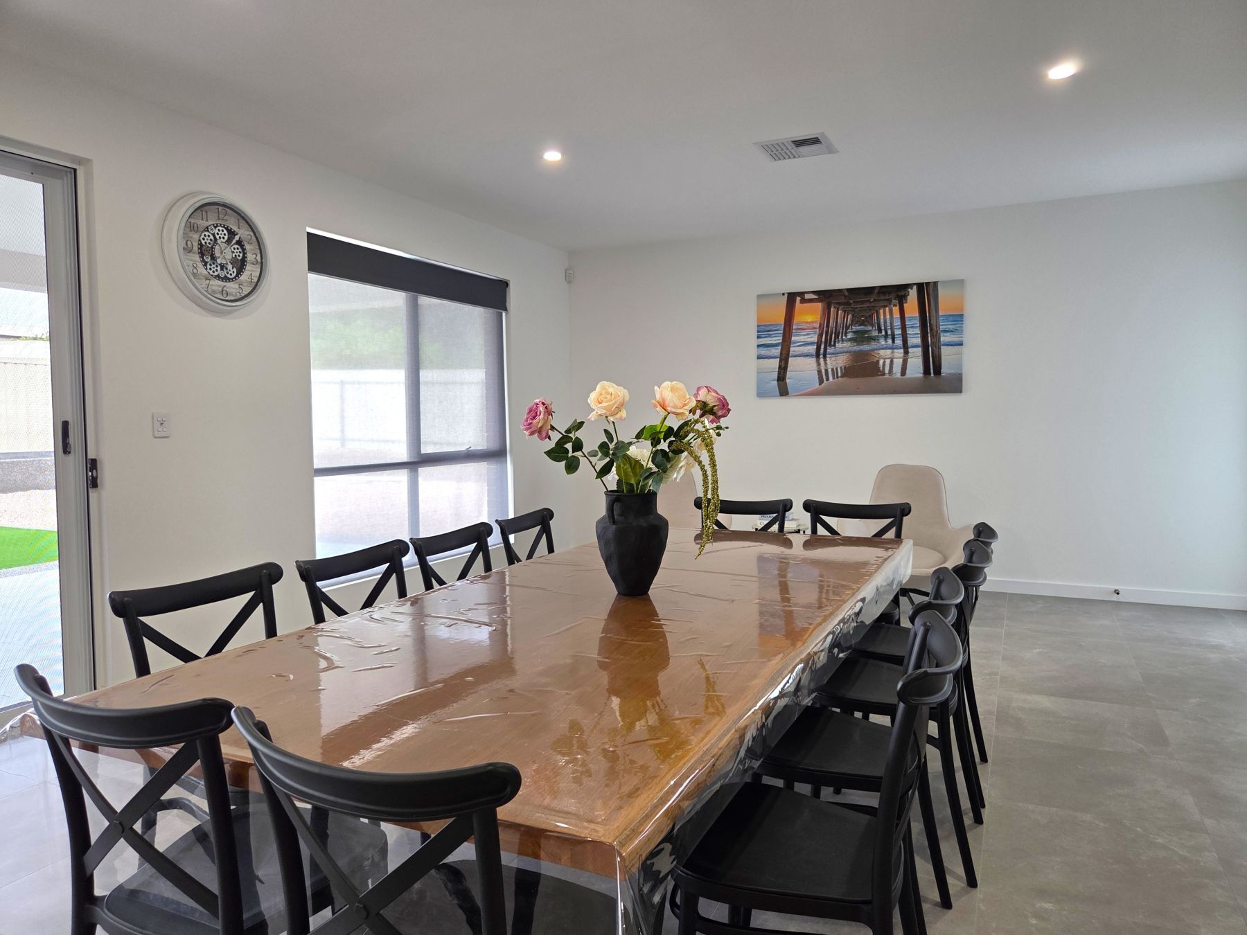A conference room with a long table, chairs, a vase with flowers, a clock, and a painting on the wall.