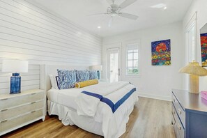 A bedroom with a bed, bedside tables, a ceiling fan, and artwork on the walls. - Palmilla Beach CocoLoco| Gulf Views | Resort Perks (Port Aransas)