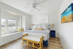 A bedroom with a bed, a window seat, a ceiling fan, a nightstand, and a painting. - Palmilla Beach CocoLoco| Gulf Views | Resort Perks (Port Aransas)