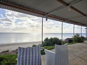 Un espace extérieur abrité, aménagé avec des sièges, et offrant une vue sur la plage et l’océan.