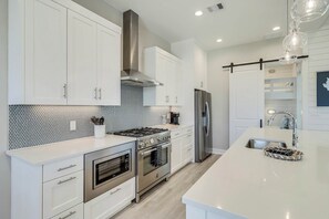 Een moderne keuken met witte kastjes, roestvrijstalen apparatuur, een betegelde spatwand en een centraal keukenblok met een spoelbak.