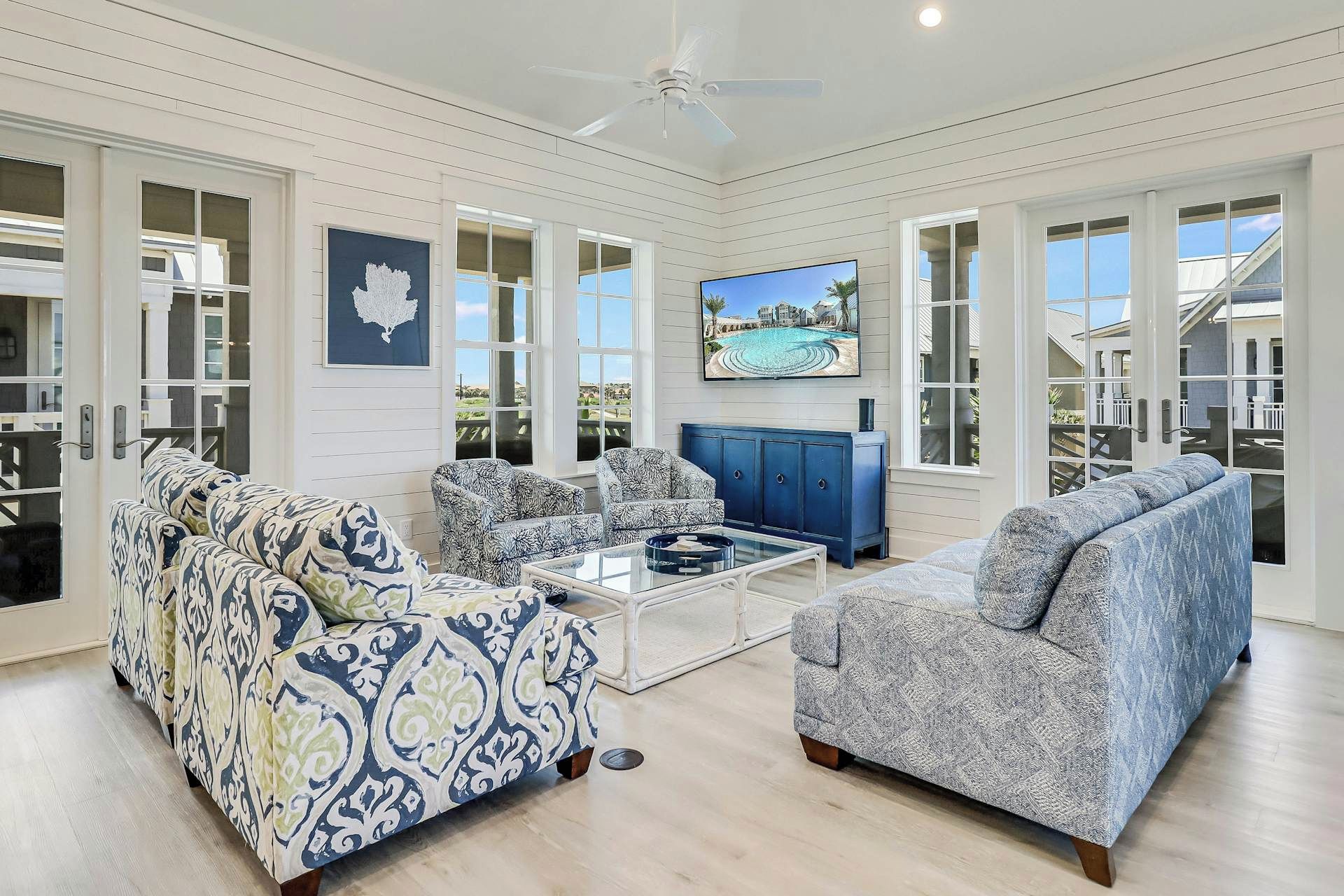 A spacious living room with a ceiling fan, large windows, and a flat-screen TV.