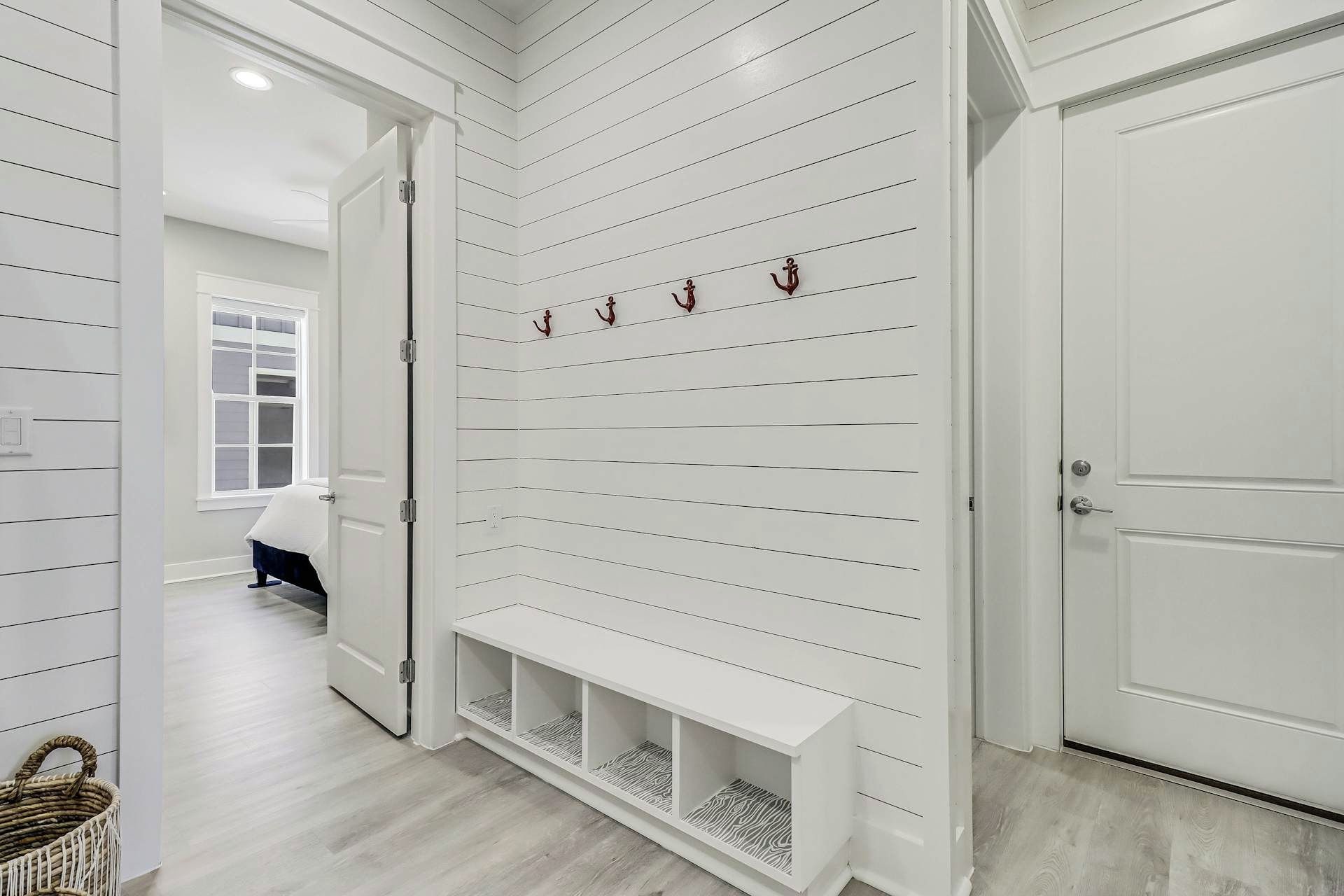 A hallway with white paneled walls, a bench, and a door.