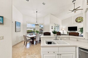 A modern kitchen with a dining area, a large window, and a ceiling fan. - Cape Coral Waterfront Escape | Close to Shopping & Dining | Heated Pool, Private Dock & Gulf Access (Cape Coral)