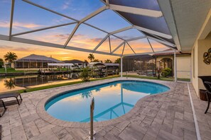 A swimming pool with a clear view of the sunset, surrounded by a covered patio area with a view of the water. - Cape Coral Waterfront Escape | Close to Shopping & Dining | Heated Pool, Private Dock & Gulf Access (Cape Coral)