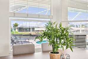 A room with a view of a swimming pool, a dining table with chairs, and a potted plant. - Cape Coral Waterfront Escape | Close to Shopping & Dining | Heated Pool, Private Dock & Gulf Access (Cape Coral)
