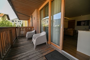 A wooden balcony with two white chairs, a sliding glass door leading to a room with a bed and a TV. - Zell City Exclusive Lodges TOP 3, balcony (Zell am See)