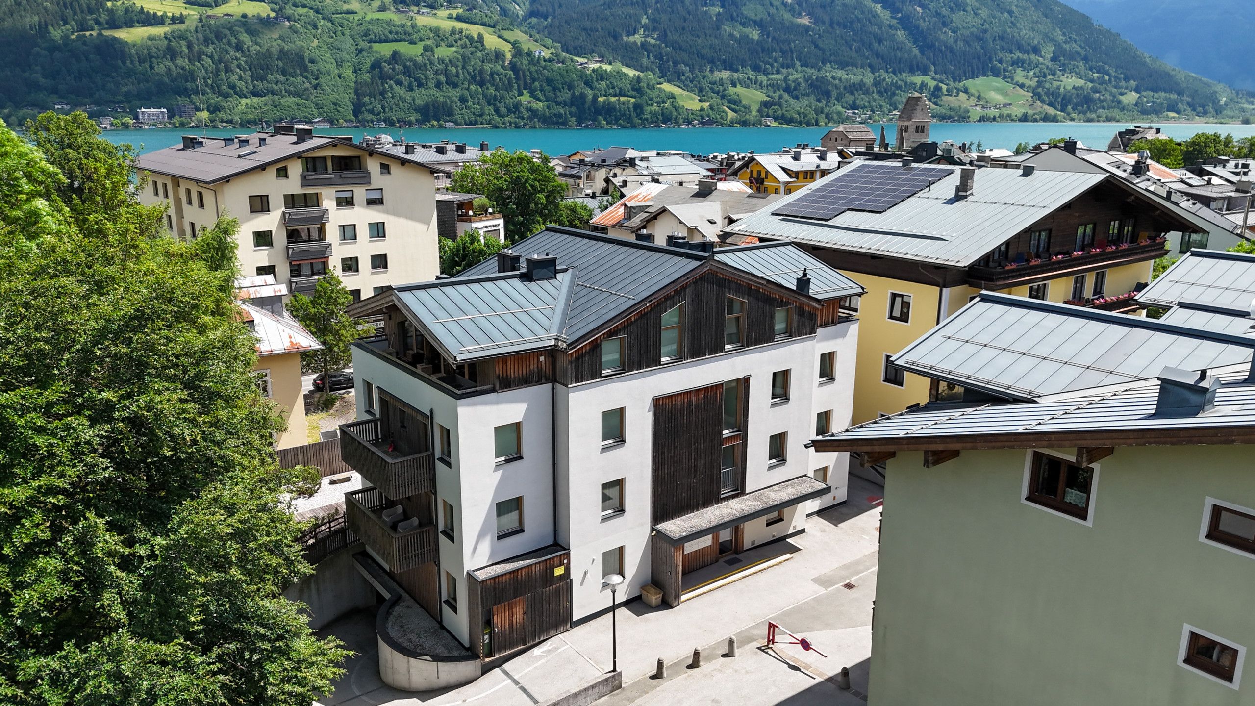 A residential area with modern buildings, a lake, and a forested hillside in the background.