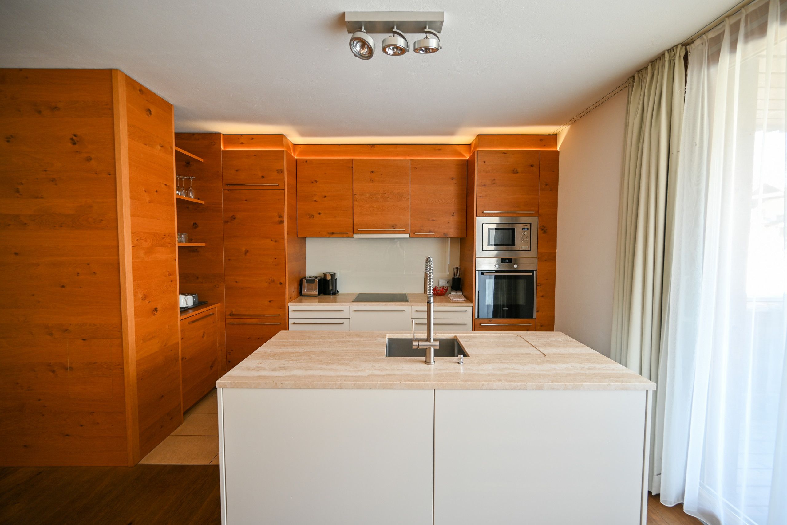 Une cuisine moderne avec des meubles en bois, un îlot central et des appareils électroménagers intégrés, notamment un four à micro-ondes et un four traditionnel.