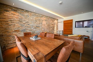 A modern dining area with a wooden table and leather chairs, a stone wall, and a wooden door. - Zell City Exclusive Lodges TOP 3, balcony (Zell am See)